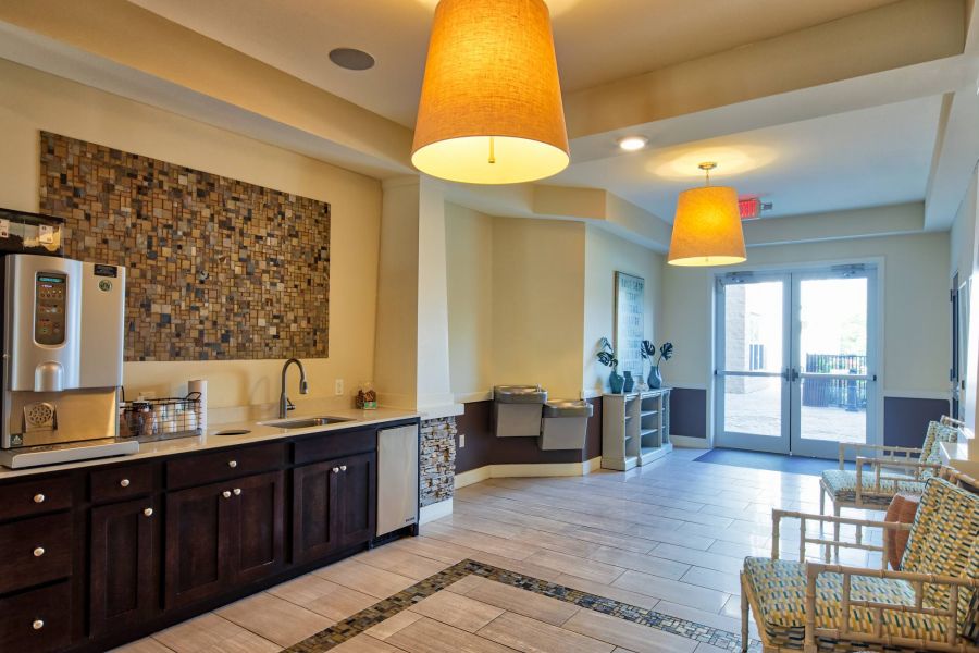 Solace Apartments A coffee station with a sink and chairs in a bright, modern lobby area near glass doors.