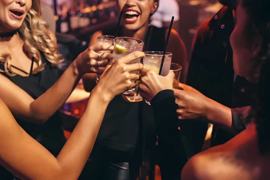 Solace Apartments Four friends in a bar clinking drinks and laughing together, enjoying a night out.