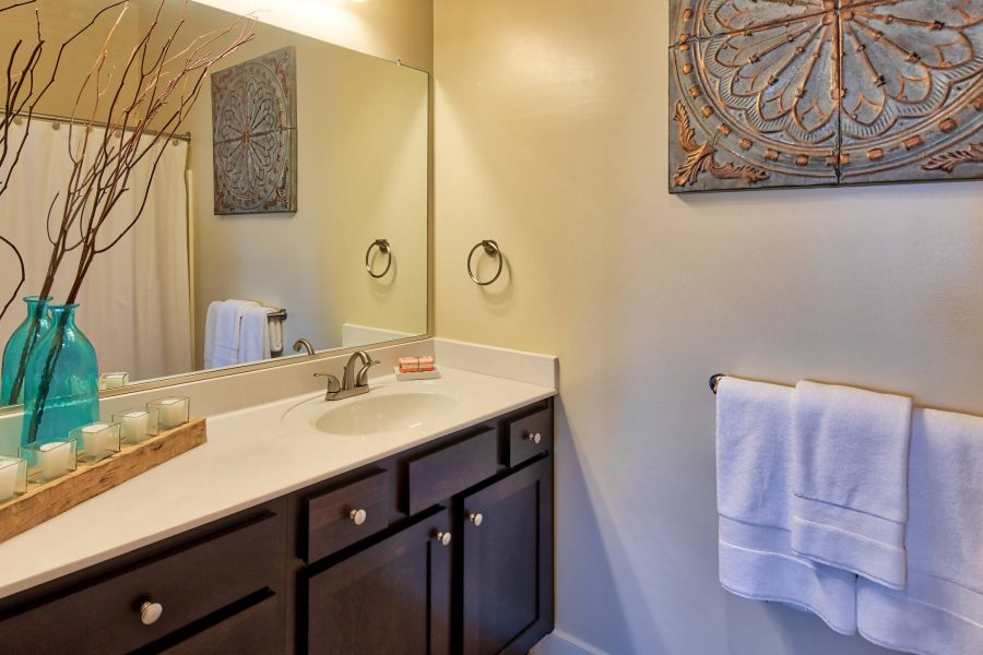 Solace Apartments Modern bathroom with dark wood cabinets, white countertop, blue vases, wall art, and neatly folded white towels.