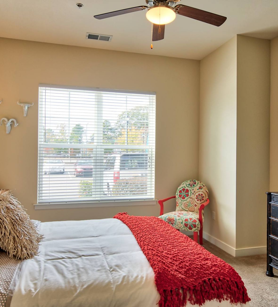 Solace Apartments Bright bedroom with a window, bed, dresser, colorful decor, and a patterned chair in the corner.