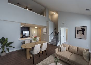Modern living and dining area with neutral tones, stairs, indoor plant, and contemporary wall art.
