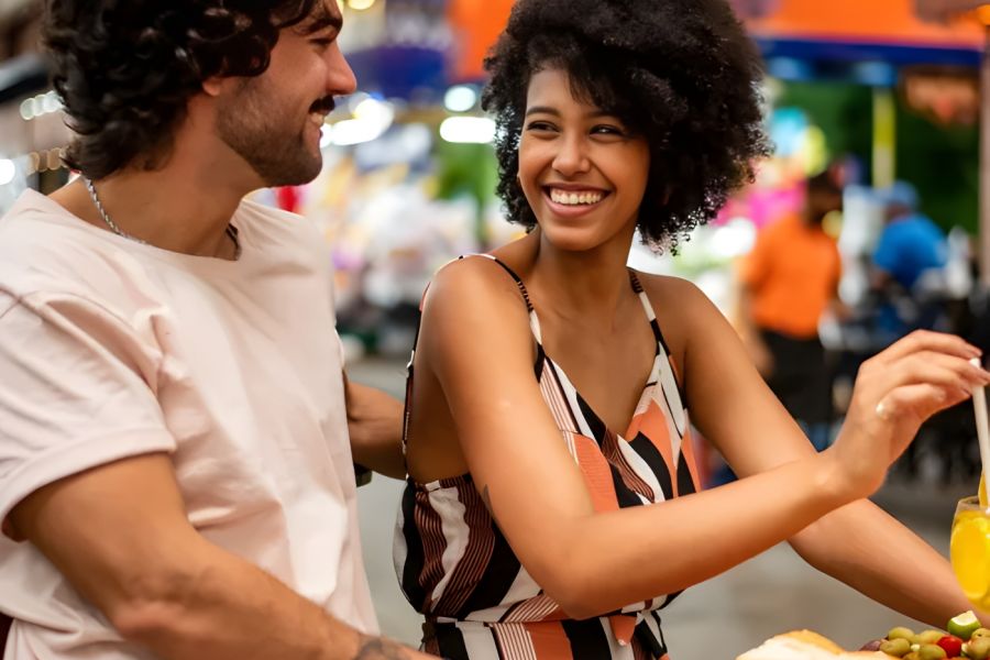 Solace Apartments A smiling couple enjoys food and drinks together at a brightly lit outdoor market.