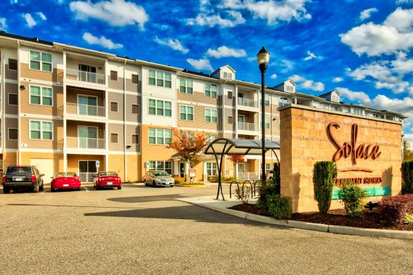 Solace Apartments Four-story apartment building with parked cars and a large entrance sign reading "Solace Apartment Homes.