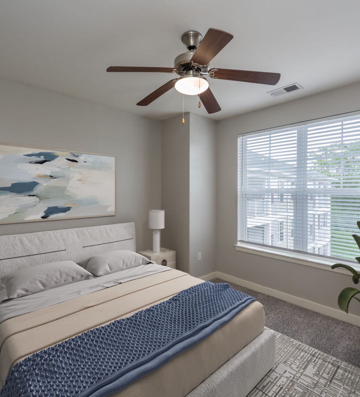 Modern bedroom with a bed, nightstands, abstract art, large window, and a potted plant in the corner.