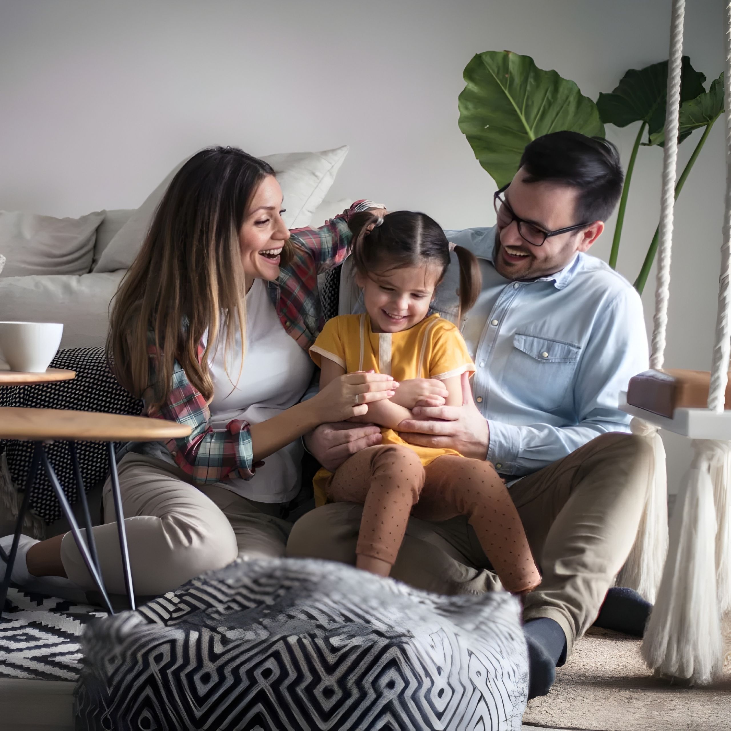Solace Apartments Smiling parents sit on the floor, hugging and playing with their young daughter in a cozy living room.