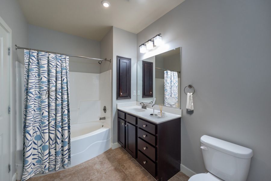 Modern bathroom with a bathtub, leaf-patterned shower curtain, vanity, mirror, and toilet.