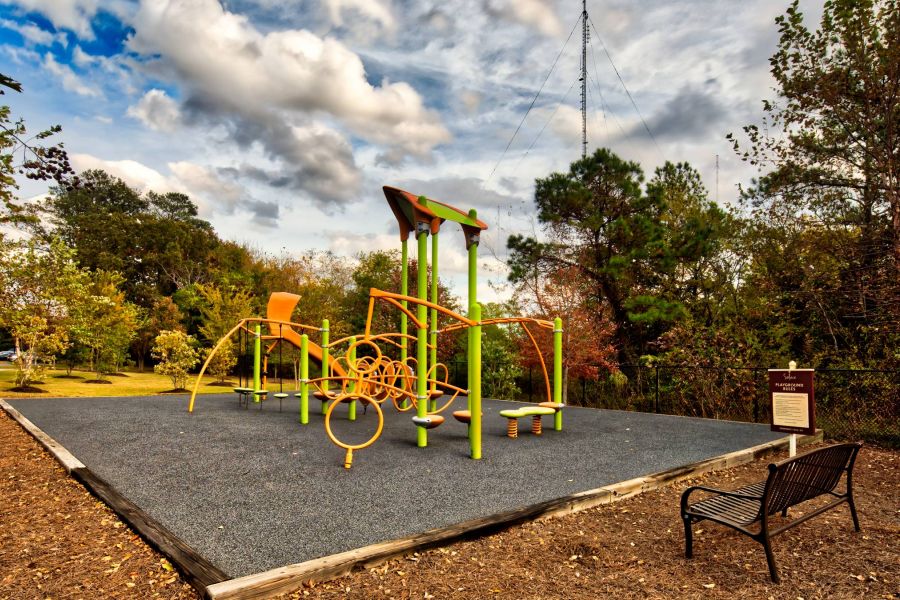 Solace Apartments Outdoor playground with colorful climbing structures, surrounded by trees, under a cloudy sky.