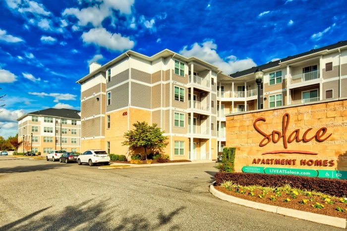 Modern apartment complex with a "Solace Apartment Homes" sign under a blue sky with scattered clouds.