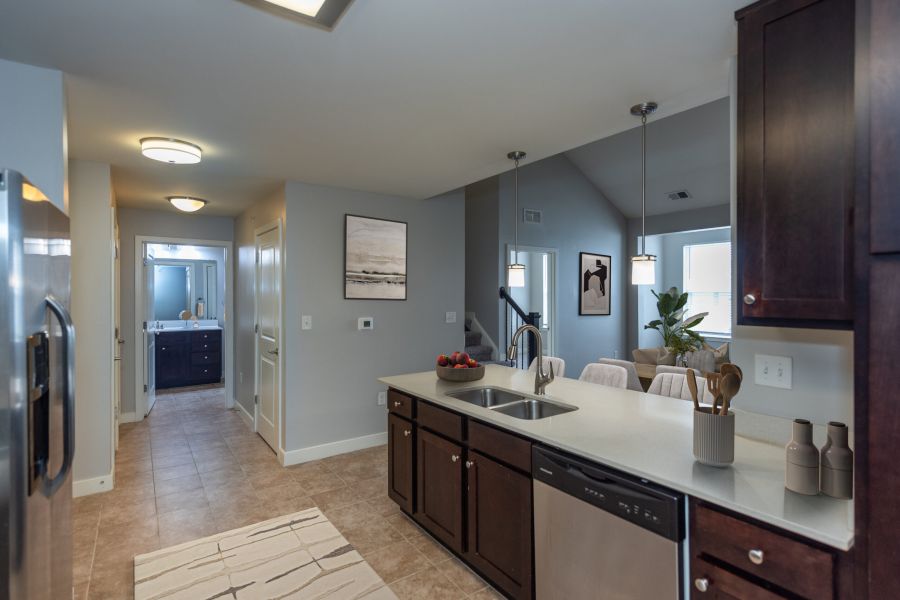 Modern kitchen with dark cabinets, light countertops, and a view into a dining and living area with natural light.