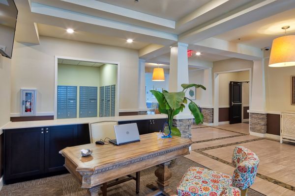 Solace Apartments A modern office lobby with a wooden desk, laptop, colorful chair, and mailboxes in the background.