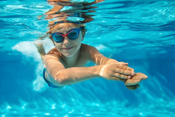 Solace Apartments Child wearing goggles swims underwater in a pool, stretching one arm forward and smiling at the camera.