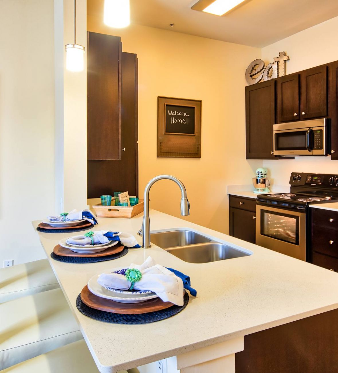 Solace Apartments Modern kitchen with stainless steel appliances, dark cabinets, island, and three place settings on a counter.