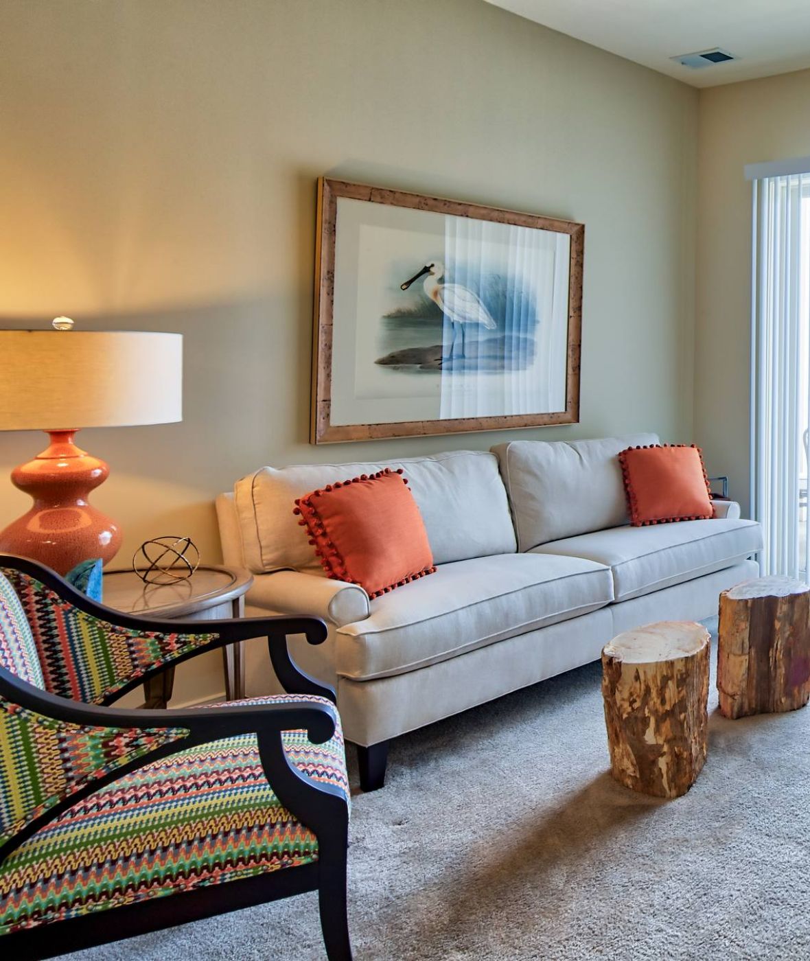 Solace Apartments Bright living room with a sofa, armchair, TV, wooden tables, and sliding glass door to outside patio.