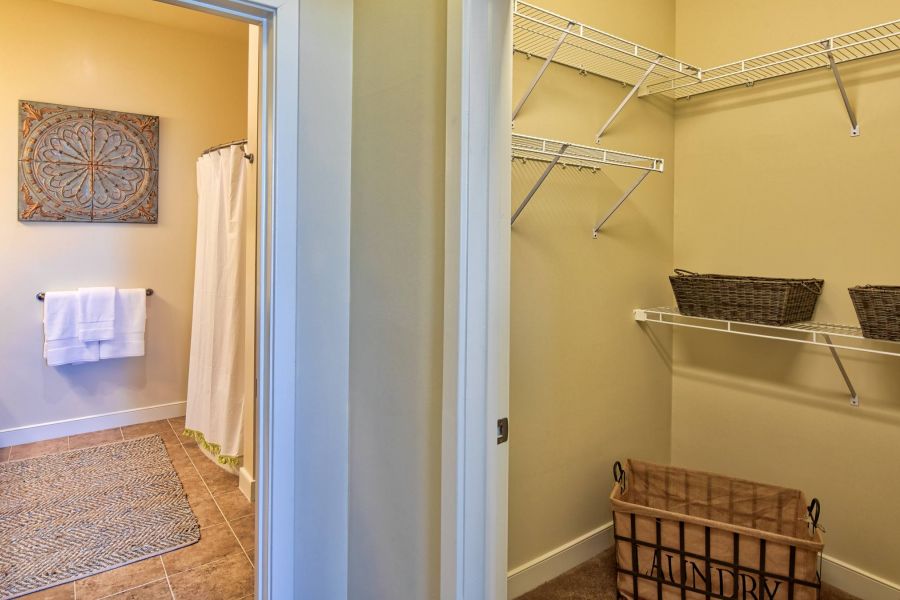Solace Apartments View of a bathroom with a shower and a connected laundry closet with shelves, baskets, and a laundry hamper.