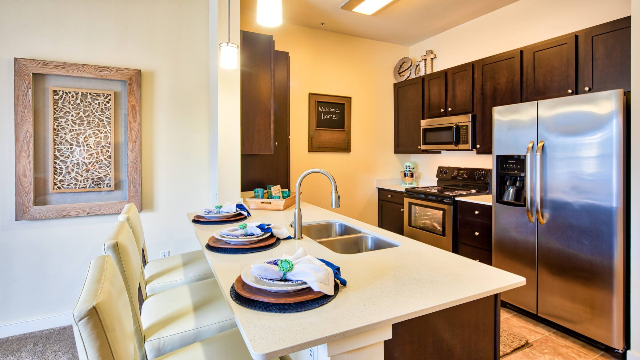 Solace Apartments Modern kitchen with stainless steel appliances, dark cabinets, island, and three place settings on a counter.