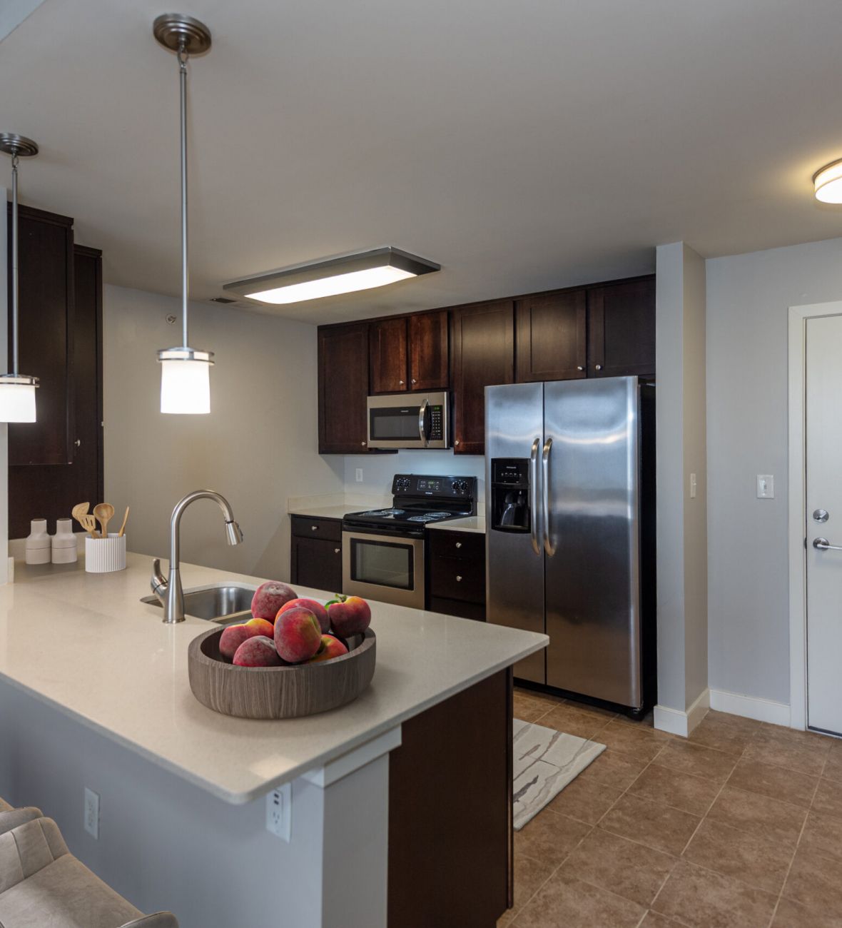 Modern kitchen with dark cabinets, stainless steel appliances, and a counter with peaches in a bowl.