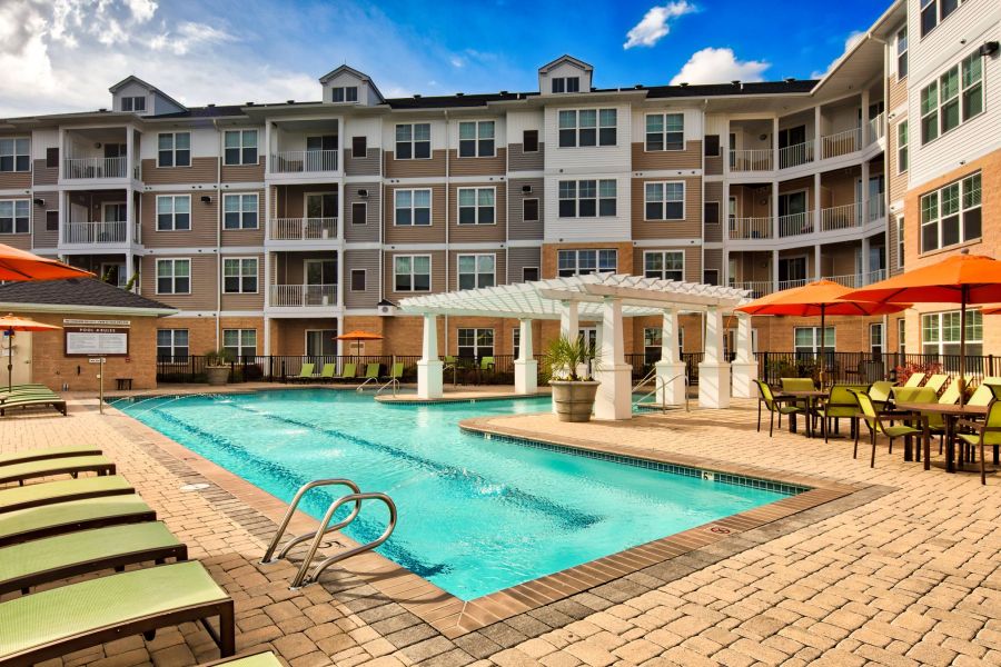 Solace Apartments Outdoor apartment pool area with lounge chairs, tables, and umbrellas in front of a multi-story building.