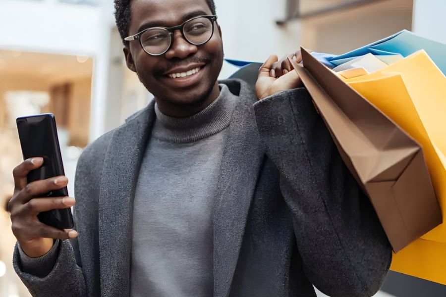 Solace Apartments Smiling man holding a phone and colorful shopping bags inside a mall.